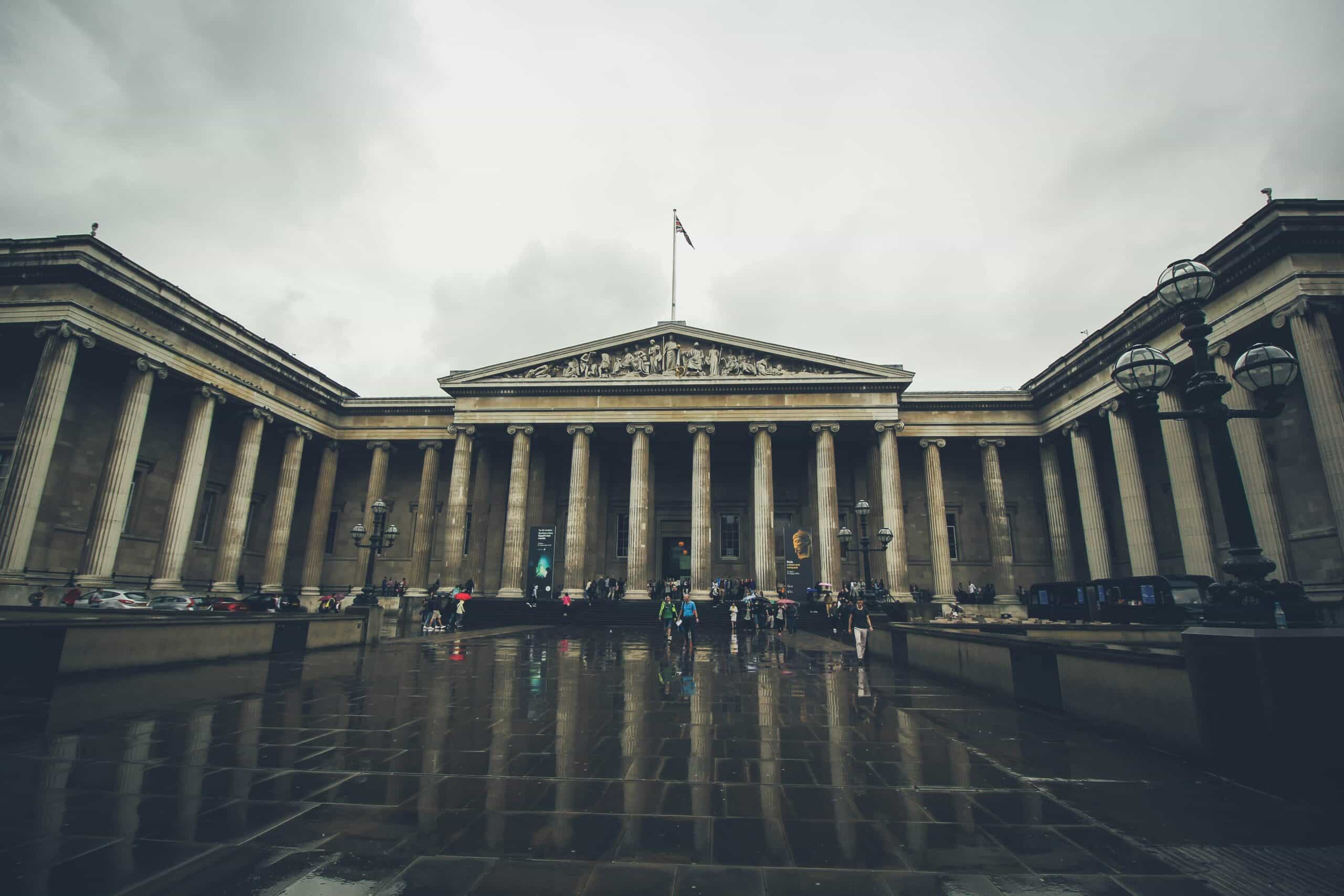 The front entrance of the British Museum in London with visitors walking in front of the historic building