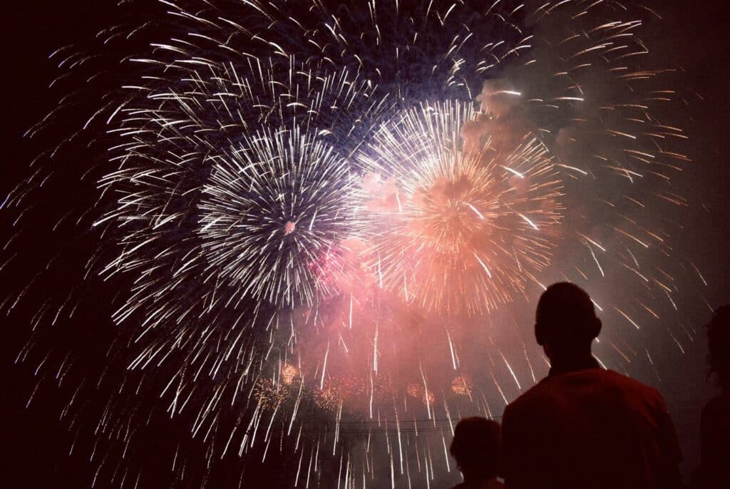 A man and his son watching a colorful fireworks display, which takes place during Honolulu’s major festivals