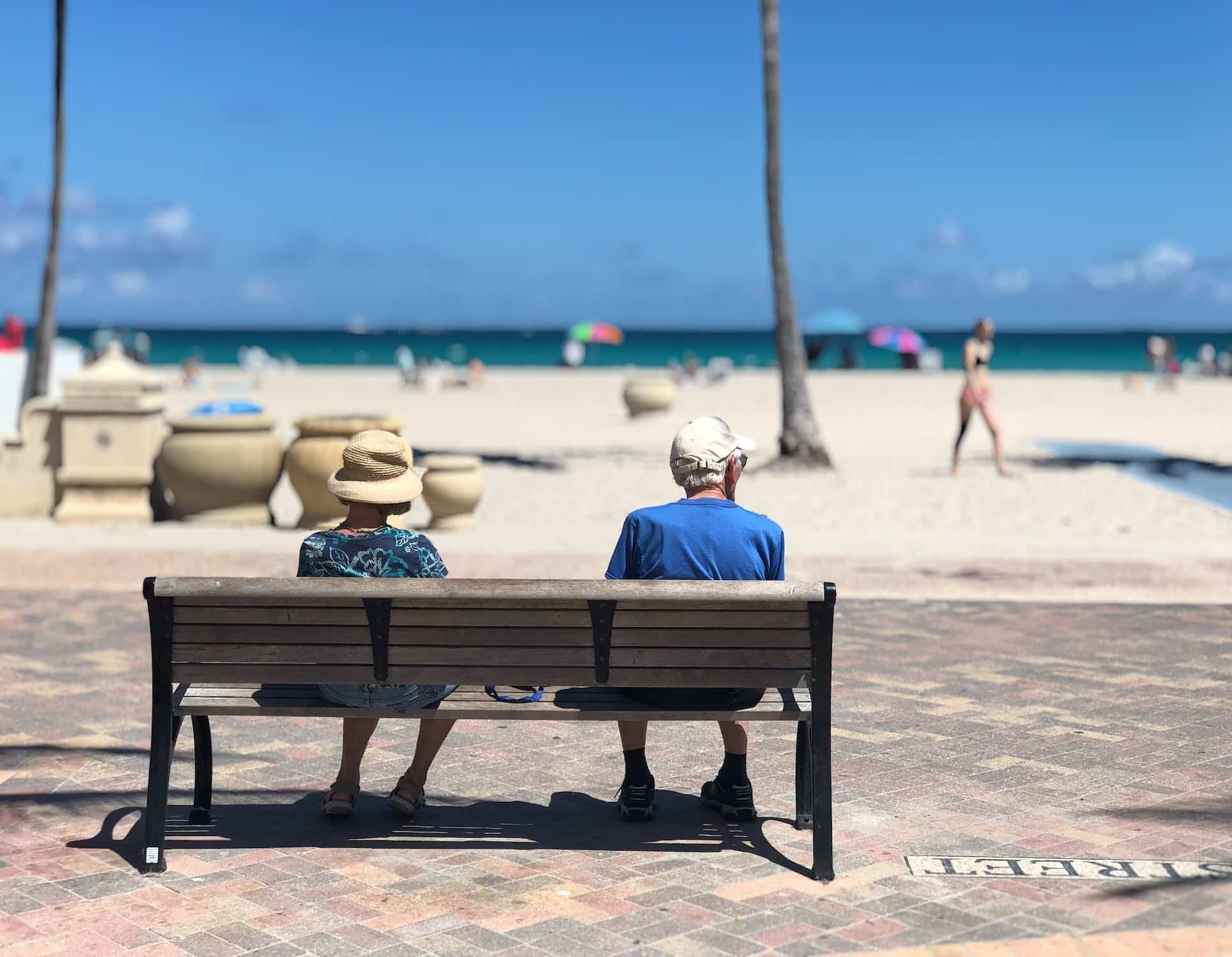 An elderly couple sitting on a bench by the beach in Florida