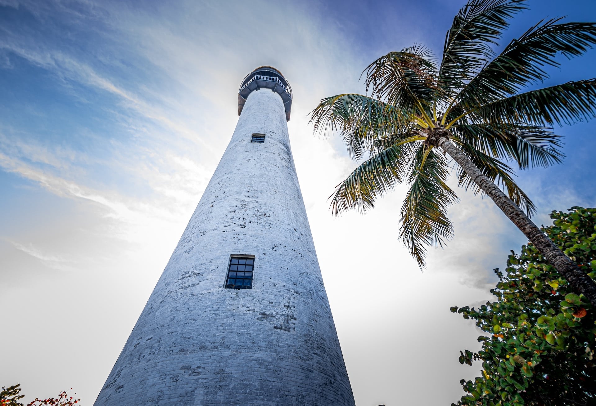 Cape Florida lighthouse with a palm tree in the background; against a blue sky with clouds.