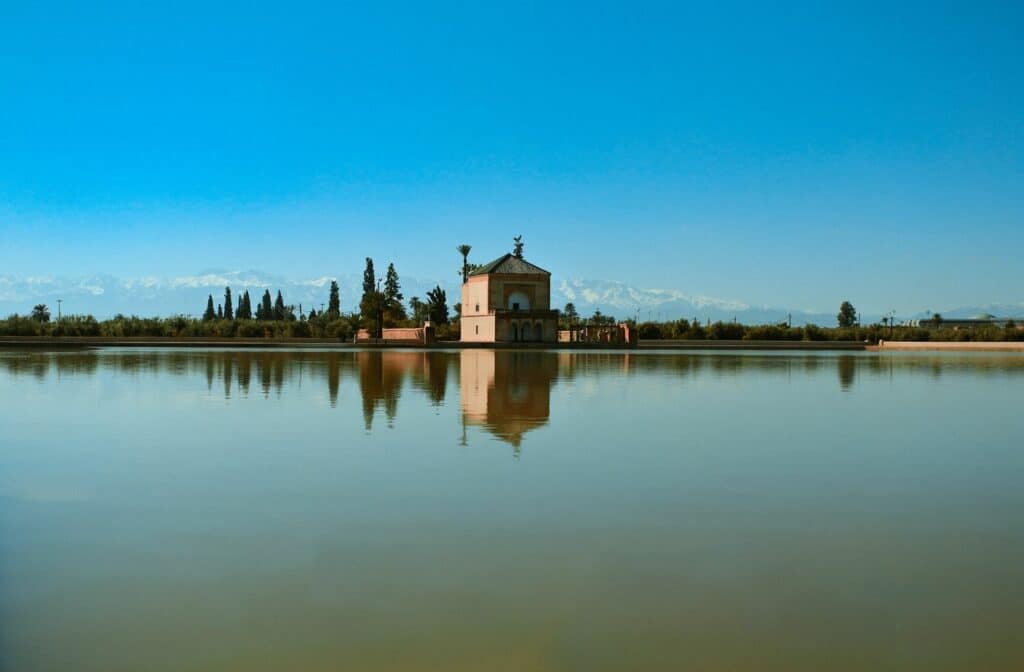 The Menara Gardens reflected in its central lake, with the High Atlas Mountains slightly visible on the horizon.